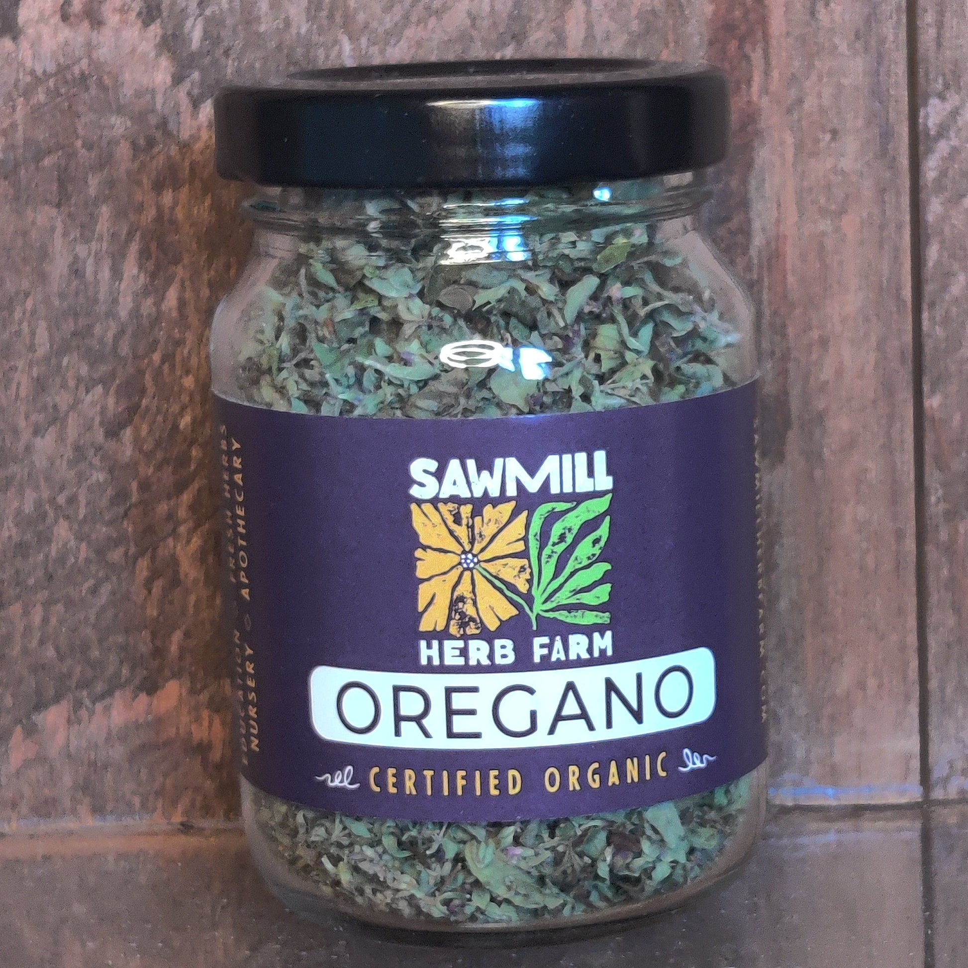 Jar of oregano with Sawmill Herb Farm label on a wooden surface